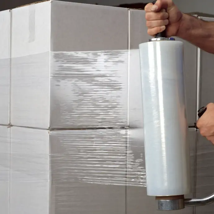 Worker wrapping stacked boxes with stretch film in a warehouse for secure packaging